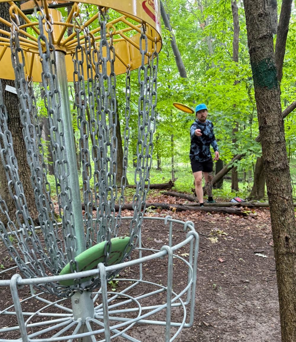 Man disc golfs in heavily wooded area.
