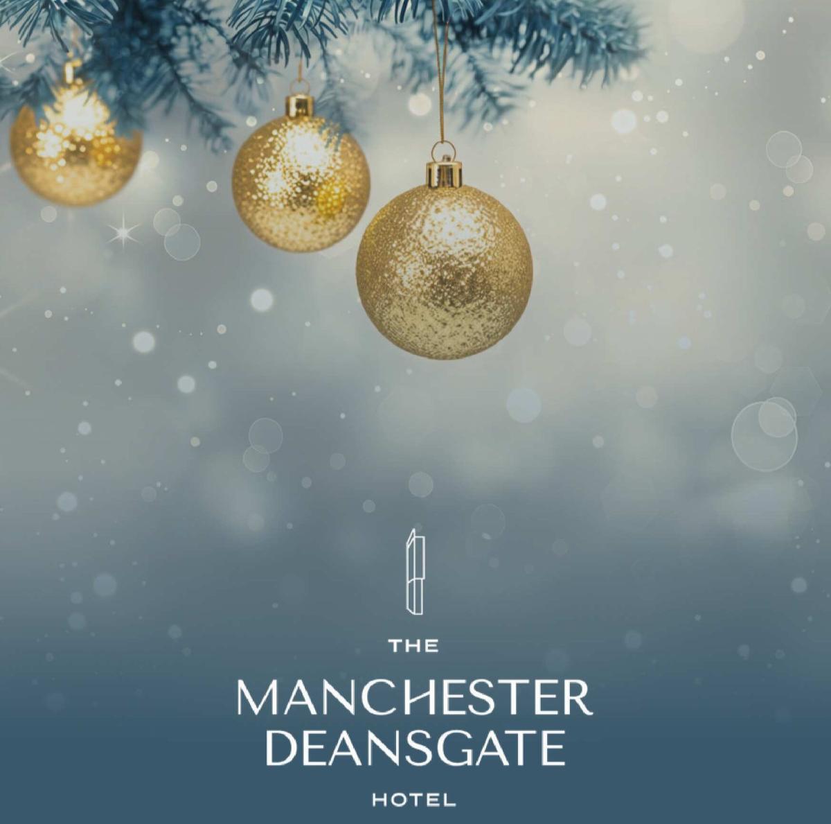 Christmas-themed promotional image for The Manchester Deansgate Hotel featuring three gold baubles hanging from frosted pine branches against a soft blue and white bokeh background, with the hotel's logo and name displayed below.