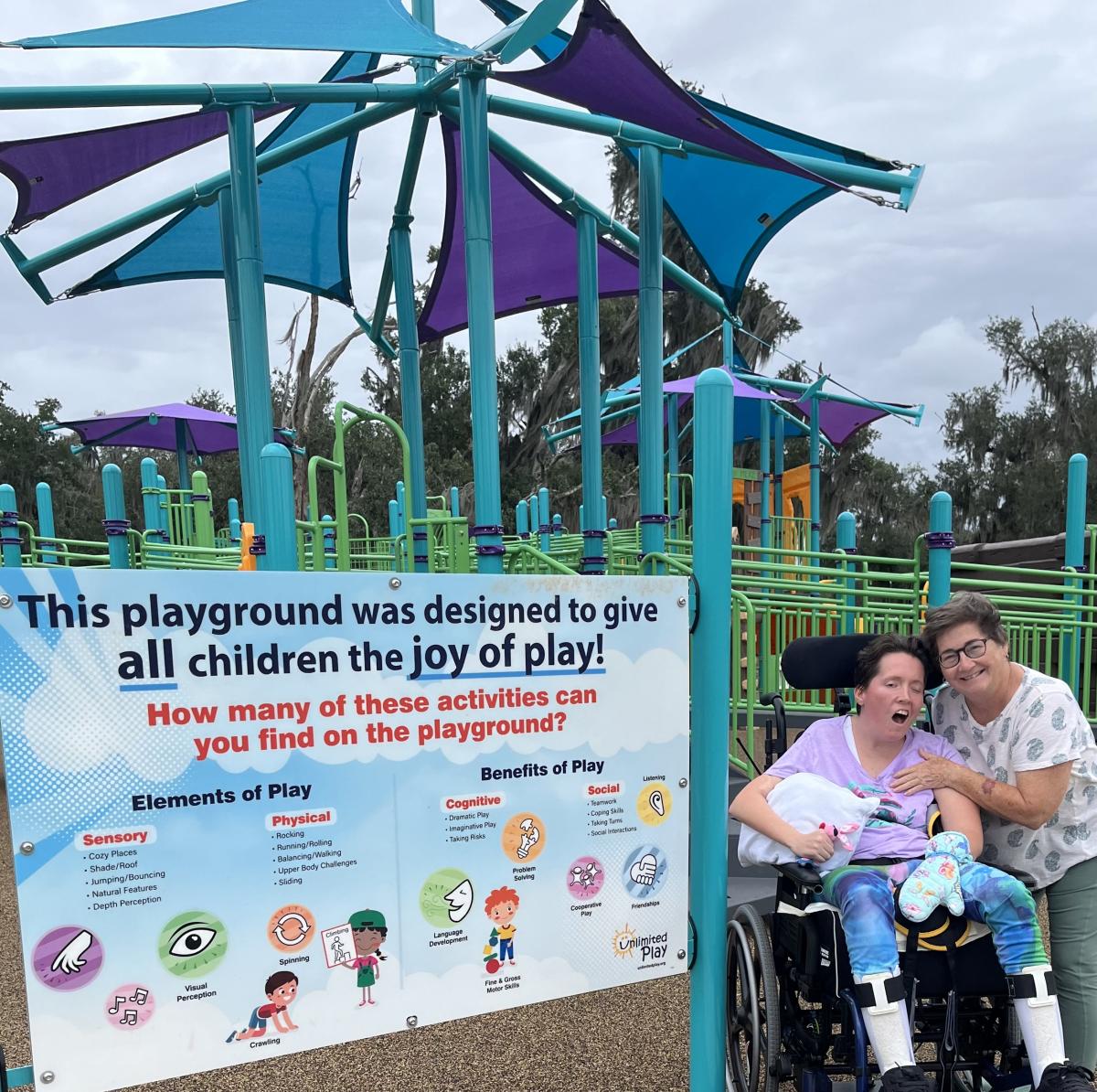 Christy and PJ smiling at the inclusive playground at Fontainebleau State Park, surrounded by accessible play equipment.