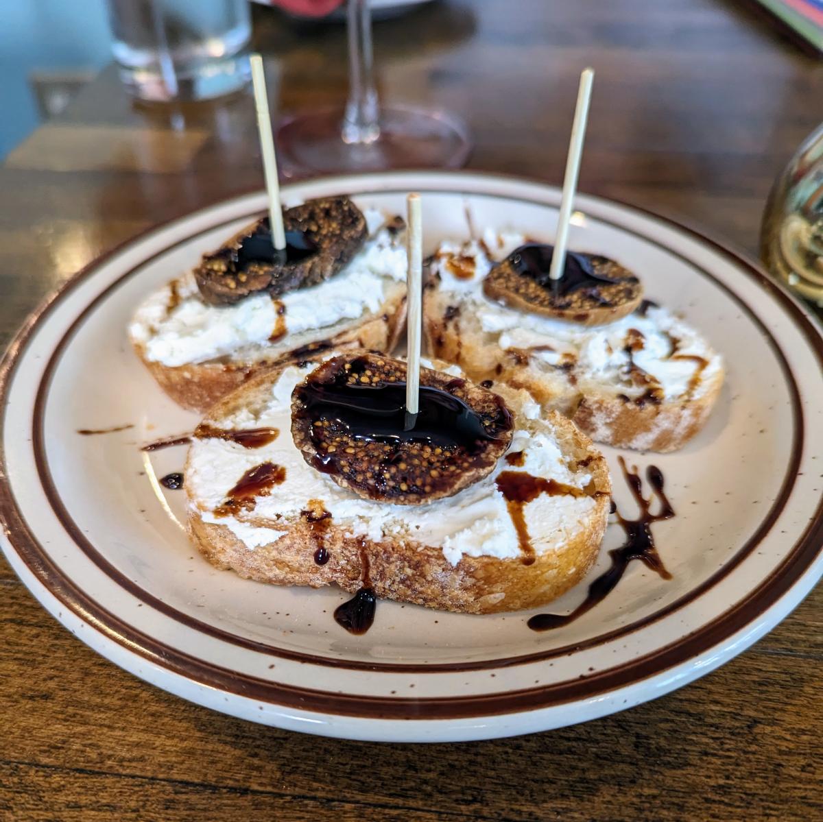 Image is of 3 baguette bread slices with sheep's milk cheese topped with dried fig and a balsamic reduction.