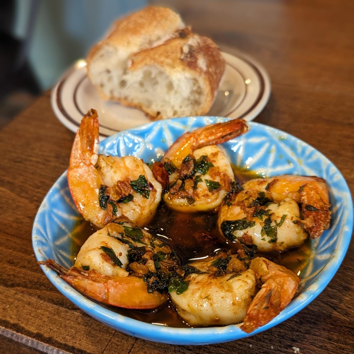 Image is a small plate, featuring shrimp, garlic, Spanish sherry, guindilla pepper and a crostini.