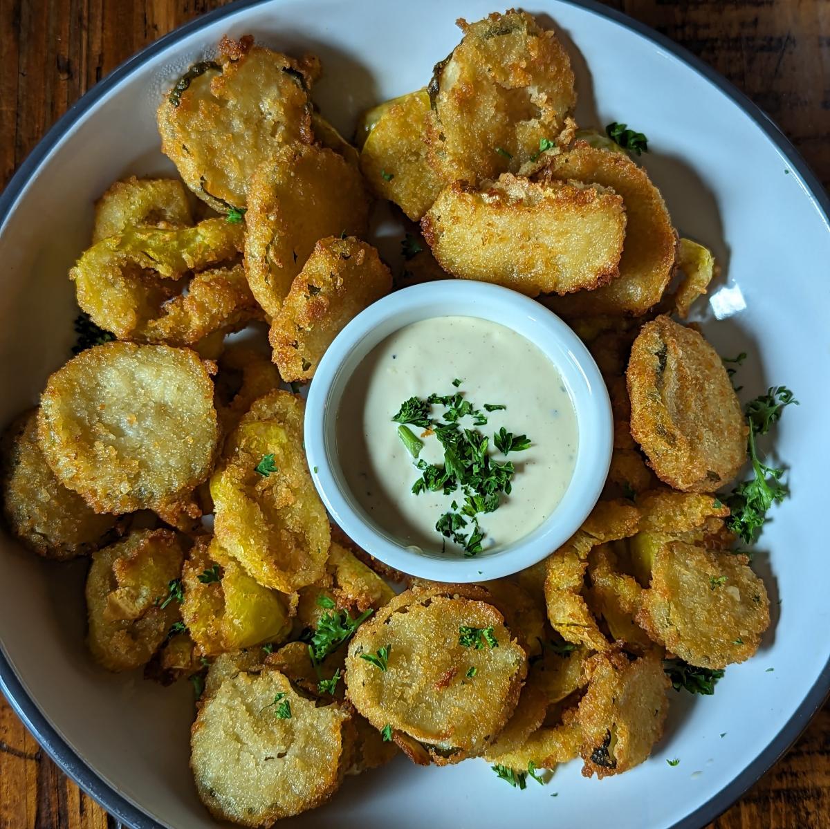 Image is of Shiner's Peter Pipers (fried pickles) in a bowl with a small cup of ranch dressing in the center.