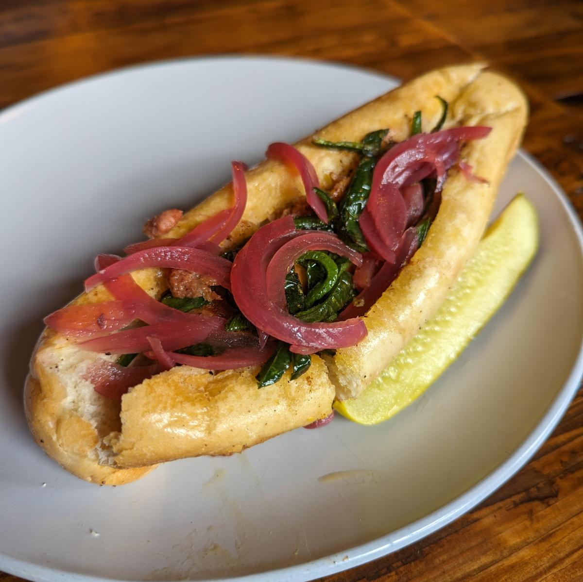 Image is of Shiners Implanted plant sausage in a toasted hot dog bun with onions and poblanos.