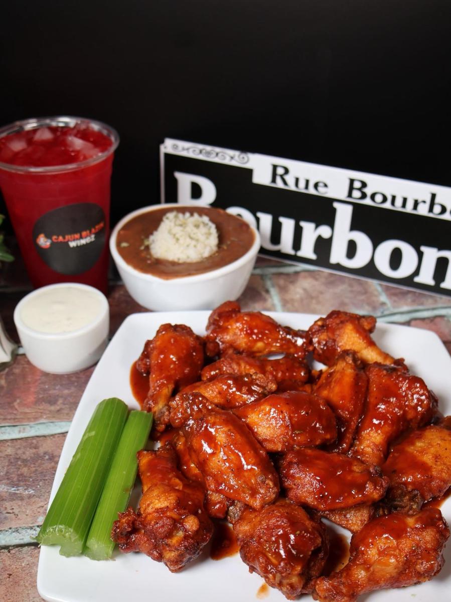 A table set with Cajun Blazin Wingz hot wings with celery and dip, gumbo and a drink. A souvenir "Rue Bourbon" street sign sits behind.