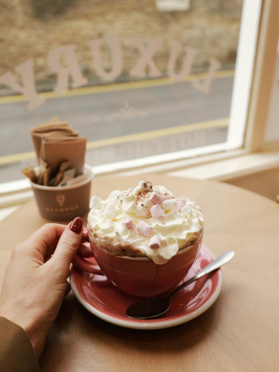 A red mug with hot chocolate topped with cream is held by a woman's hand at Alfonso Gelateria in Stow-on-the-Wold
