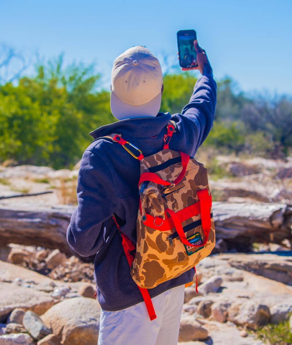 Person in outdoor gear holding up a phone for a photo in the Sonoran dessert