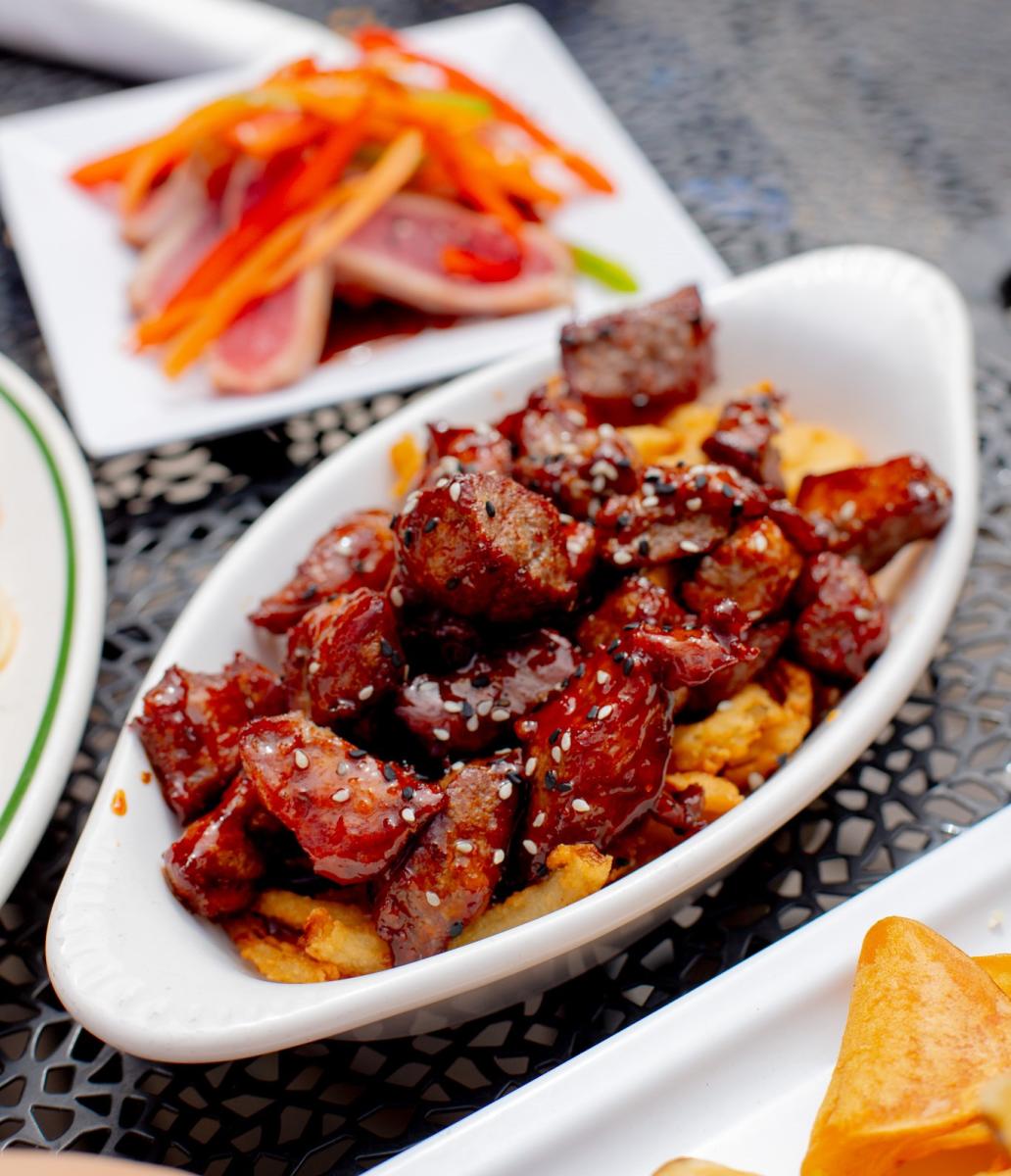 a dish of sauce covered steak bites with a dish of sliced ahi tuna in the background