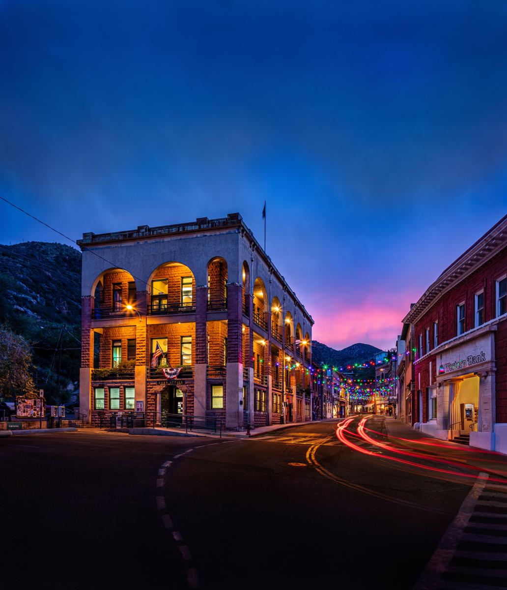 hostoric small town building at night, with dim yellow lights around the building and colorful string lights strung between the street