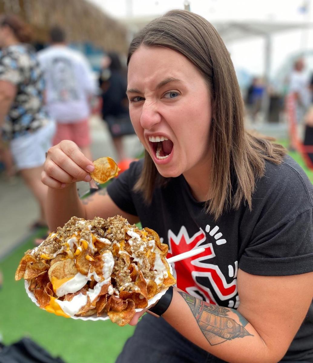 A young woman about to take a bite of goetta nachos
