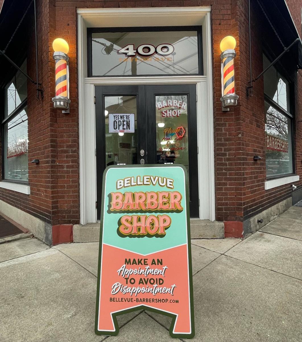 Image is of the front door of Bellevue Barbershop with a sign out front that say's "Bellevue Barber Shop".