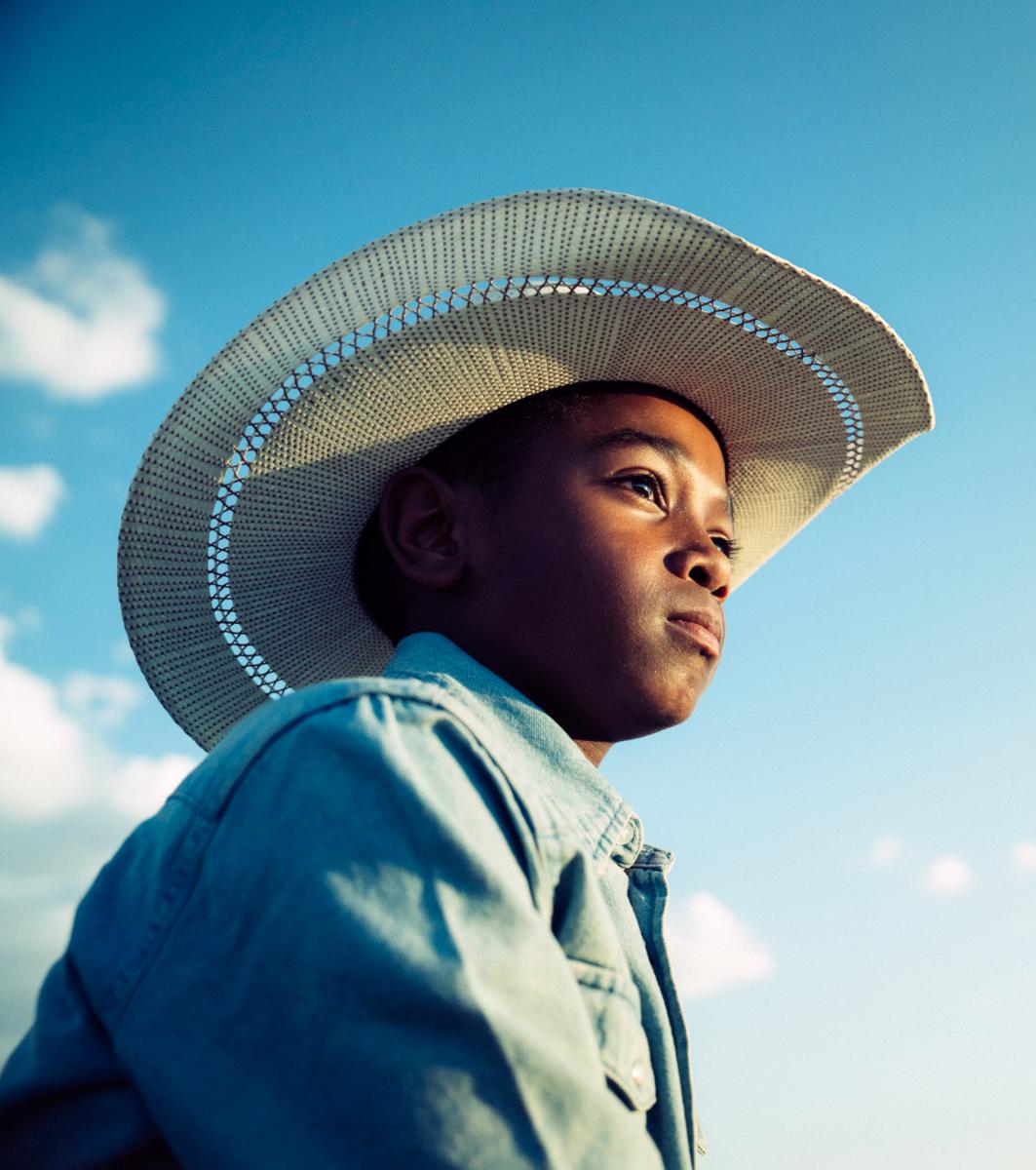 A person wearing a straw hat and denim jacket, looking pensively towards the sky with a clear blue background.
