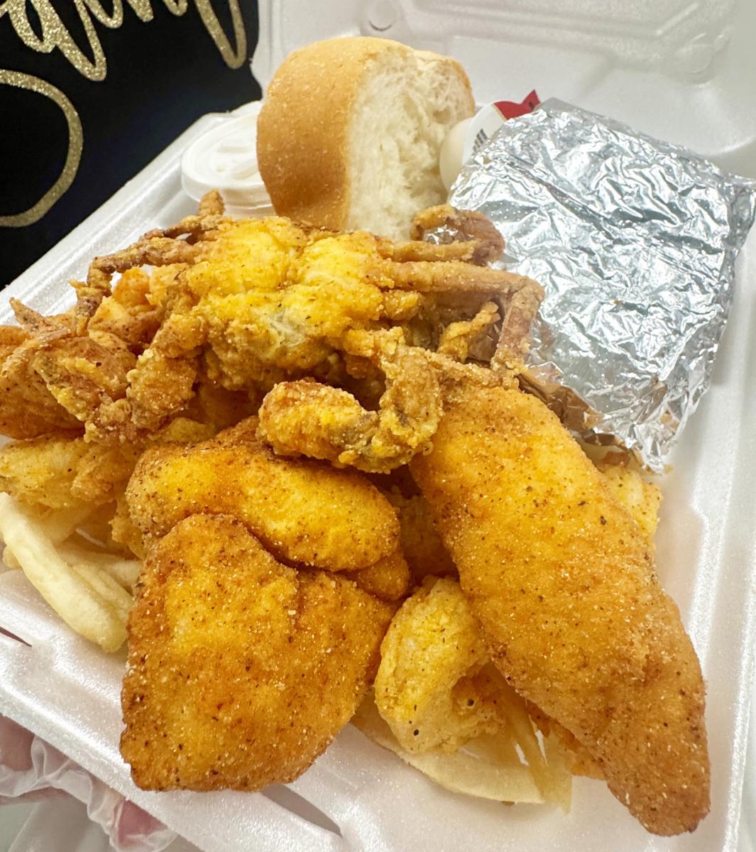 Fried soft-shelled crab, catfish and fries piled in a Styrofoam box.