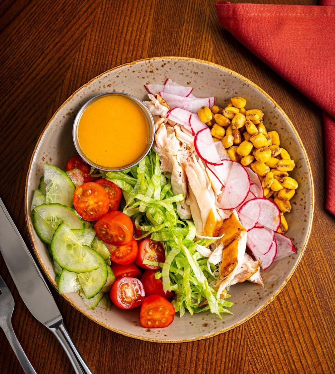 Sliced cucumbers, tomatoes, lettuce, chicken, radishes and corn line a plate to create the Chop Salad at Doma