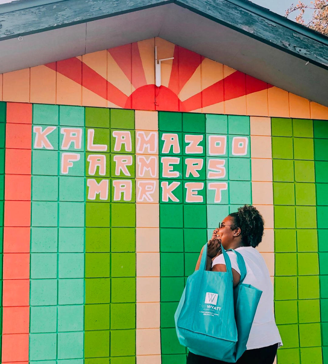 A woman walks by a mural that says "Kalamazoo Farmers Market"