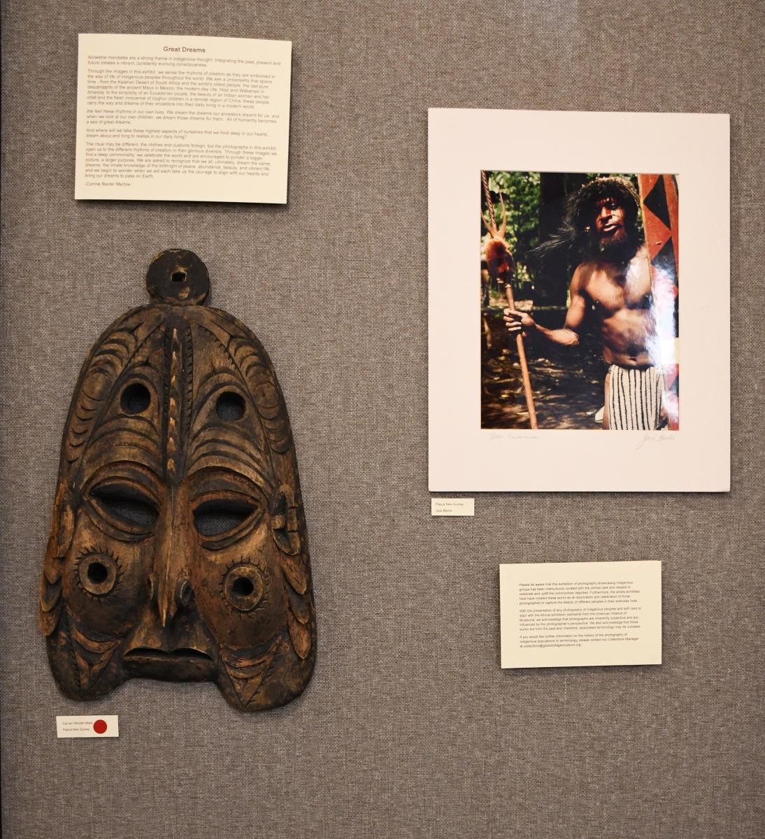 Mask on wall with photo of person with text description too small to read