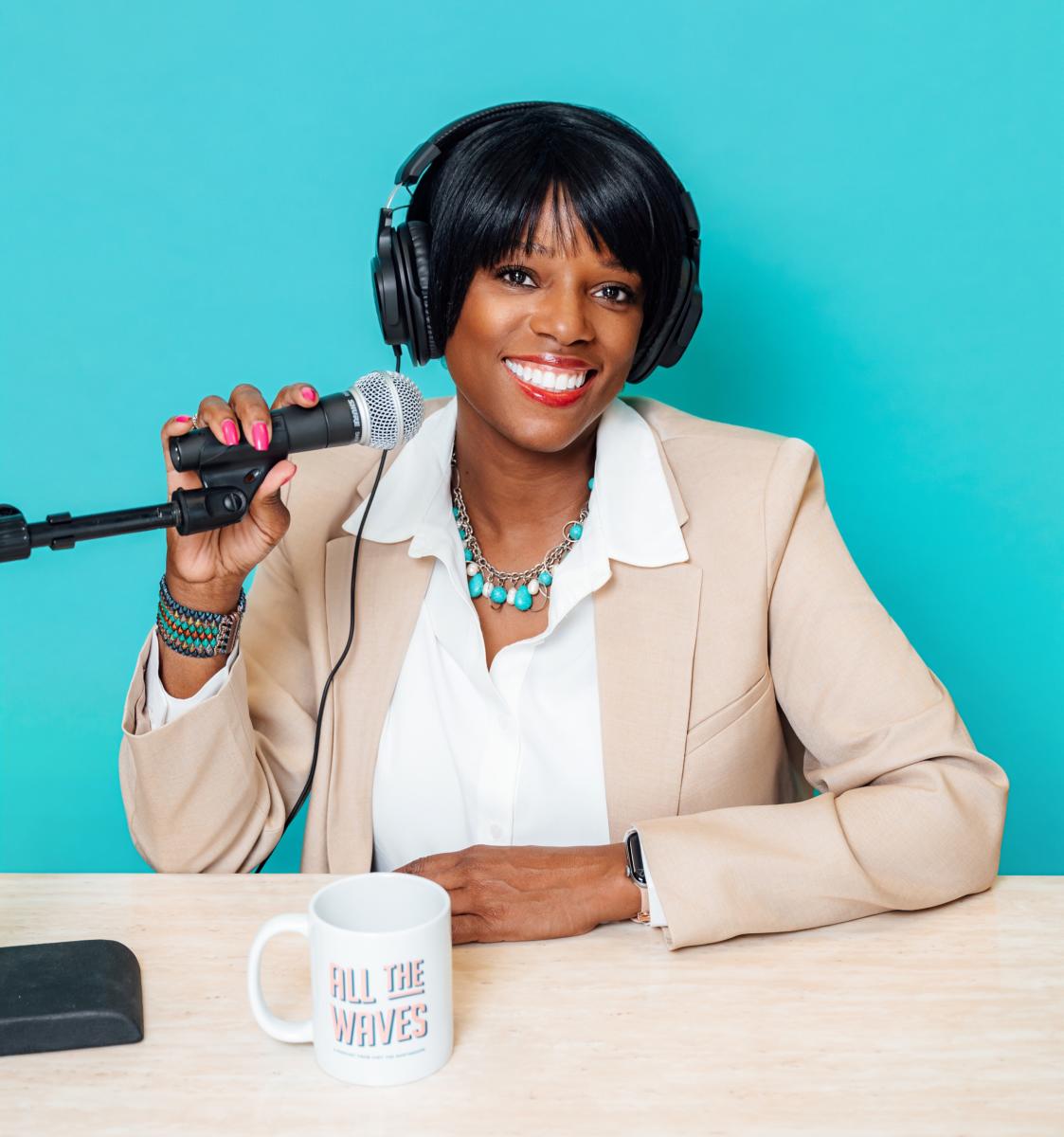 All The Waves co-host Zondra White Jones smiles while recording an episode, holding a microphone in the podcast studio.