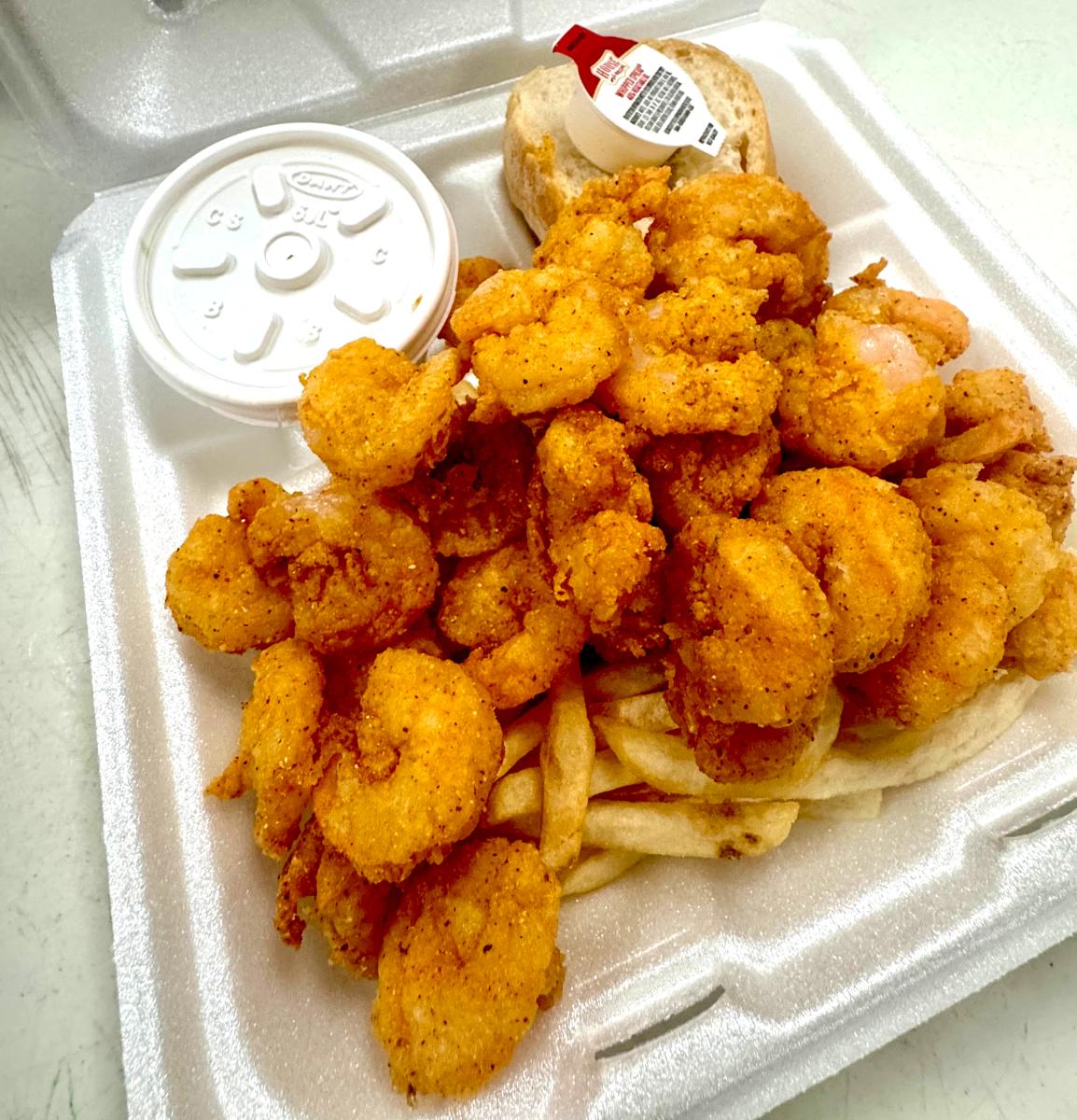 Fried shrimp, French fries and a small, white cup of dipping sauce in a Styrofoam container.