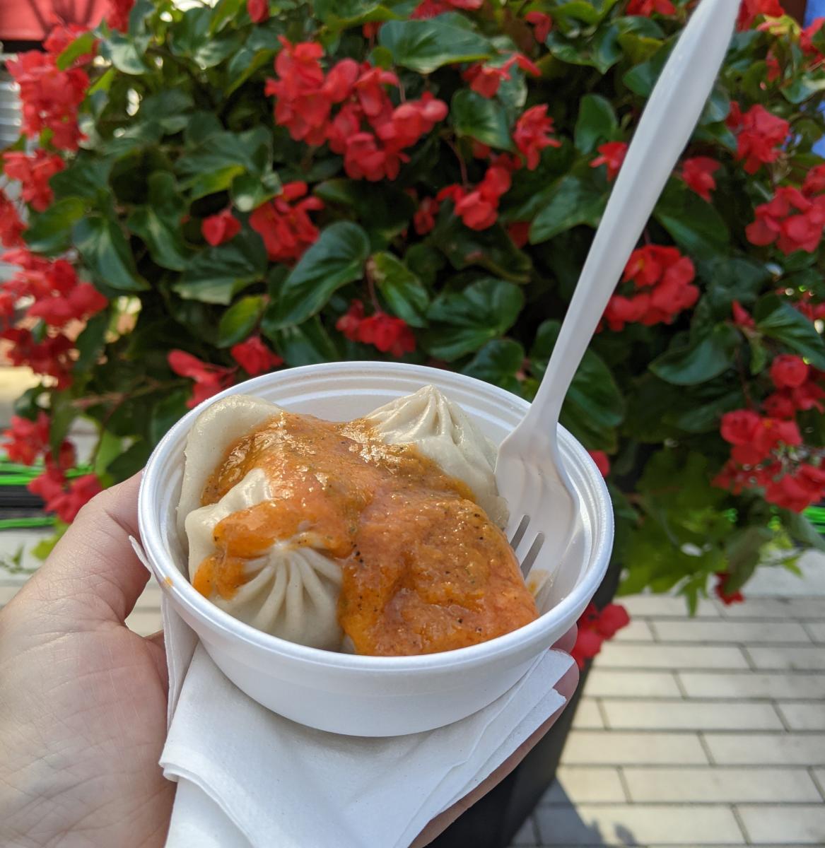 A white dish filled with momo dumplings at the Asian Food Fest in Cincinnati, OH with red flowers in the background