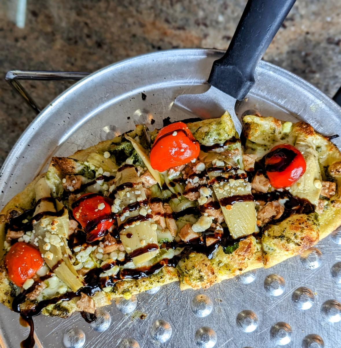 Image is of a chicken and pesto flatbread with a balsamic glaze drizzle.