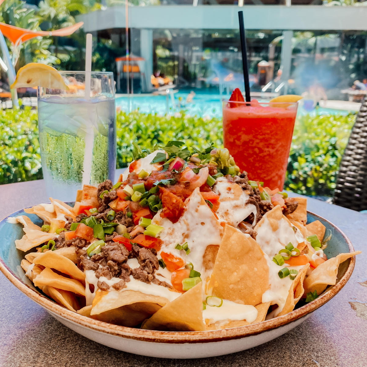 Image of a plate of nachos, glass of water, and a red, strawberry-flavored slushie beverage.