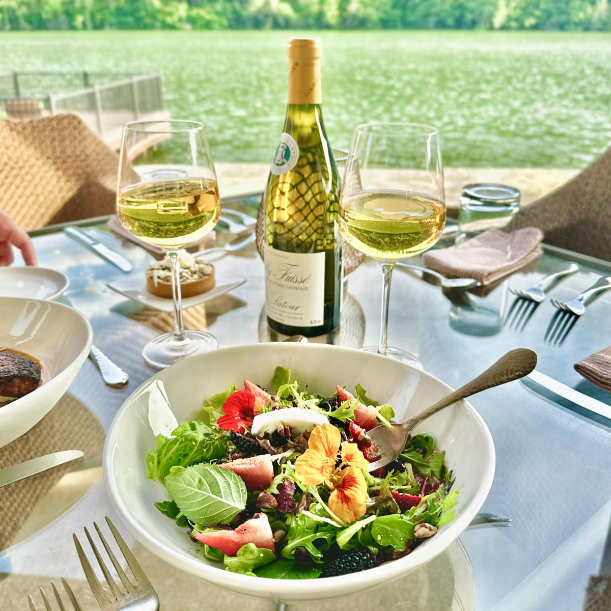 Image of a table with salad and wine glasses with a view of Lake Austin.
