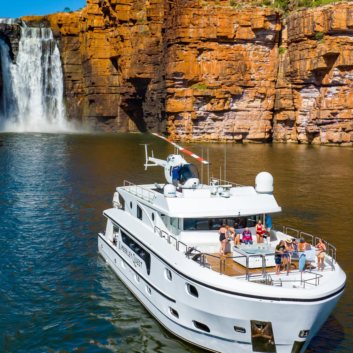 Kimberley Quest vessel and passengers on the Kimberley coast, with a waterfall visible in the background
