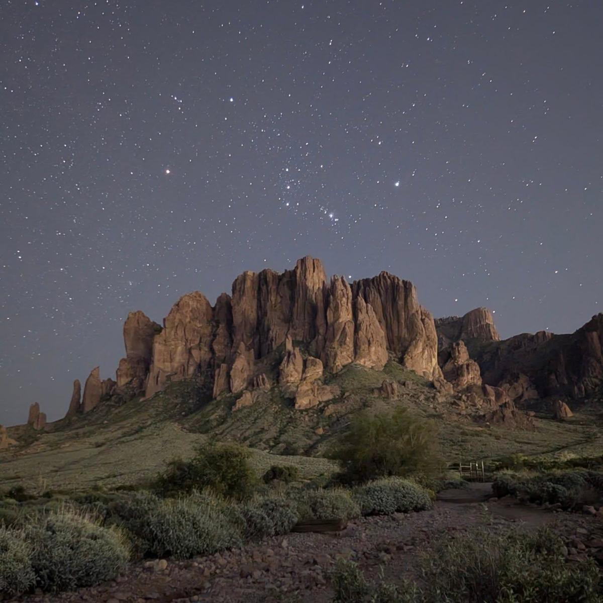 a night image of the Superstition Mountains showing the mountains aglow under a starry sky