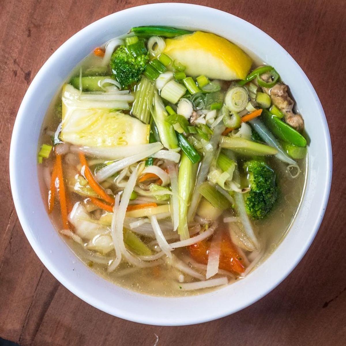 The image is a white bowl with Buddha Delight Noodle Soup with is noodle soup with green onions, celery, carrots and broccoli.
