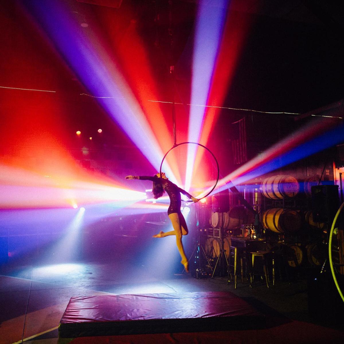 Image is of a lady doing an acrobatic routine while hanging above the ground in a hoop.