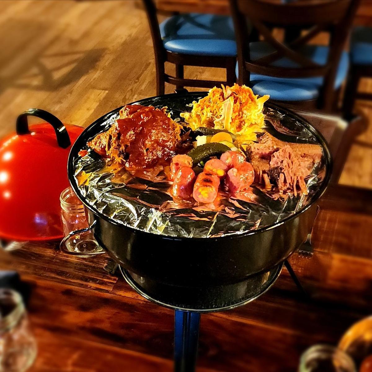 Image is of a mini grill sitting on a table. The grill contains 3 different kinds of BBQ and mets.