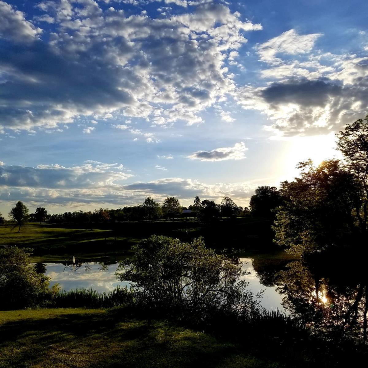 Blue sky with clouds over trees and water at Idlewild Park in Burlington, Ky.