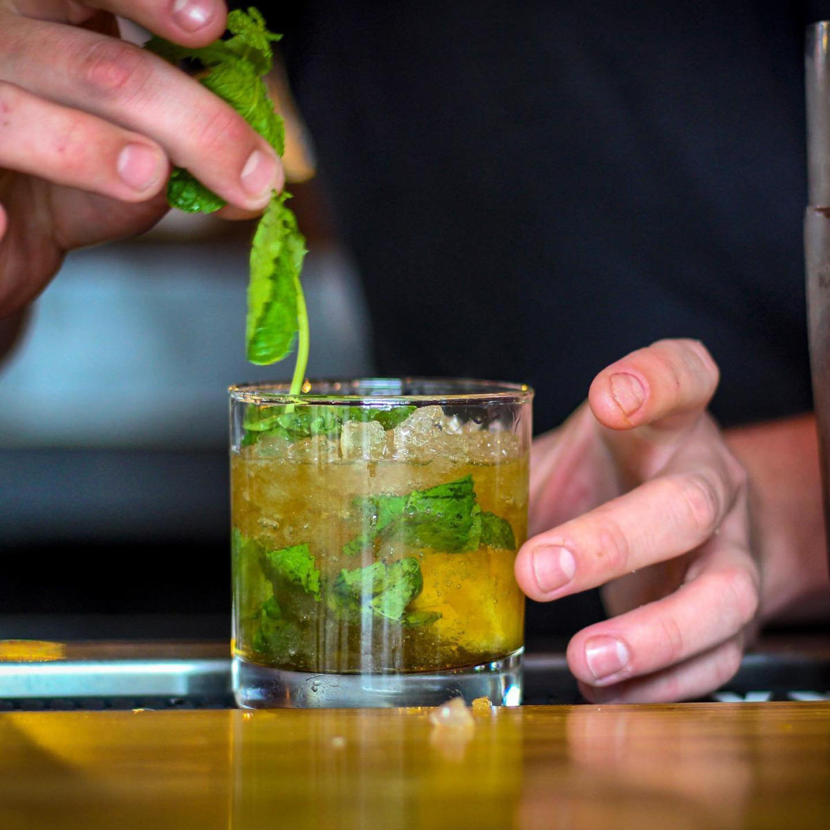 A man's hand places a sprig of mint into a mint julep cocktail on ice