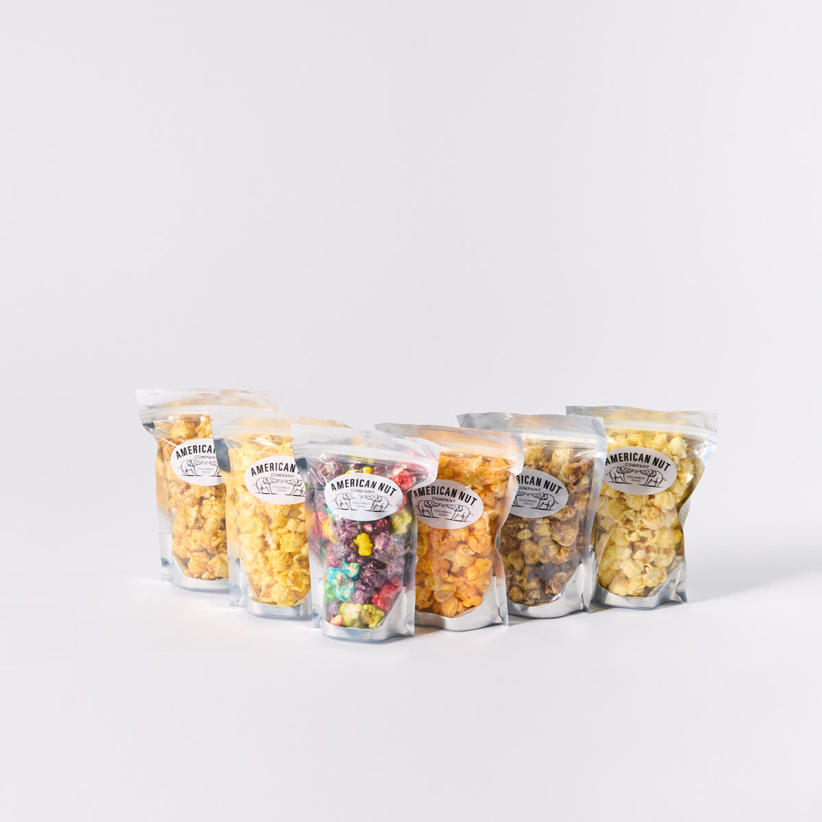 Six bags of various popcorn, all of which are included in American Nut Company's Popcorn Snack Pack
