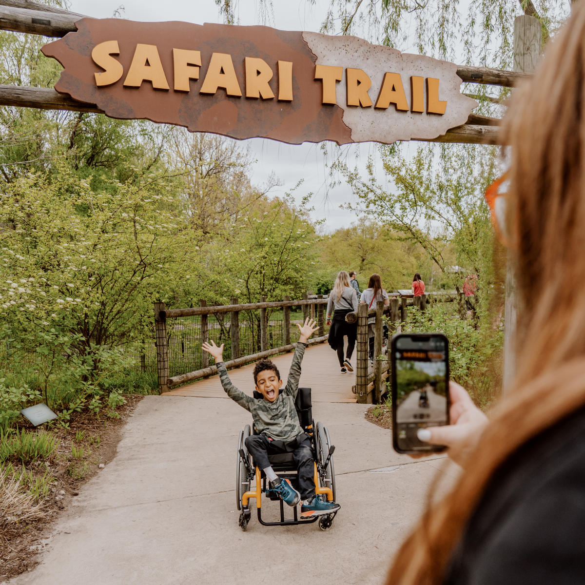 Mom taking photo of Boy in wheelchair enjoying the zoo