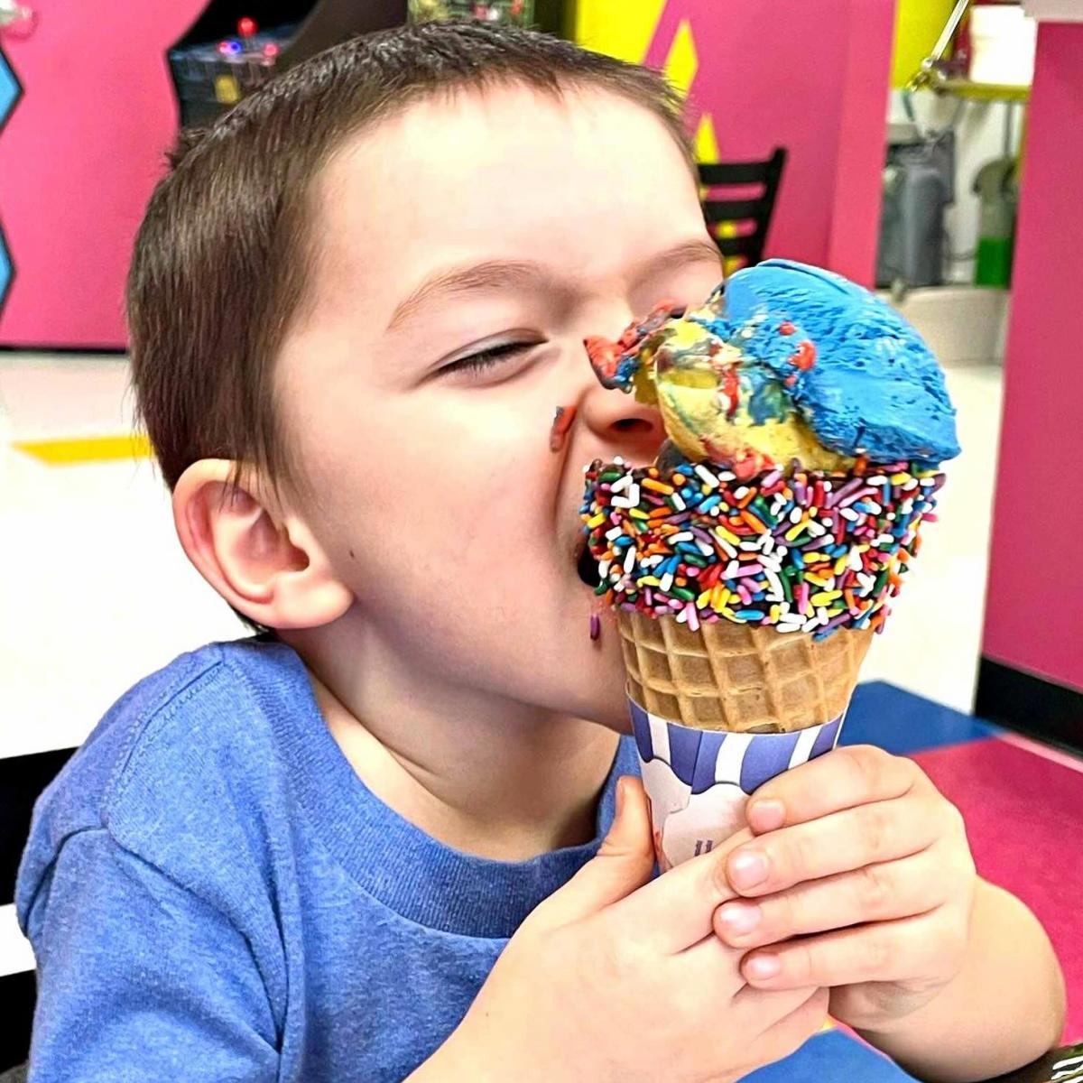 A child very messily eats a colorful, large ice cream cone