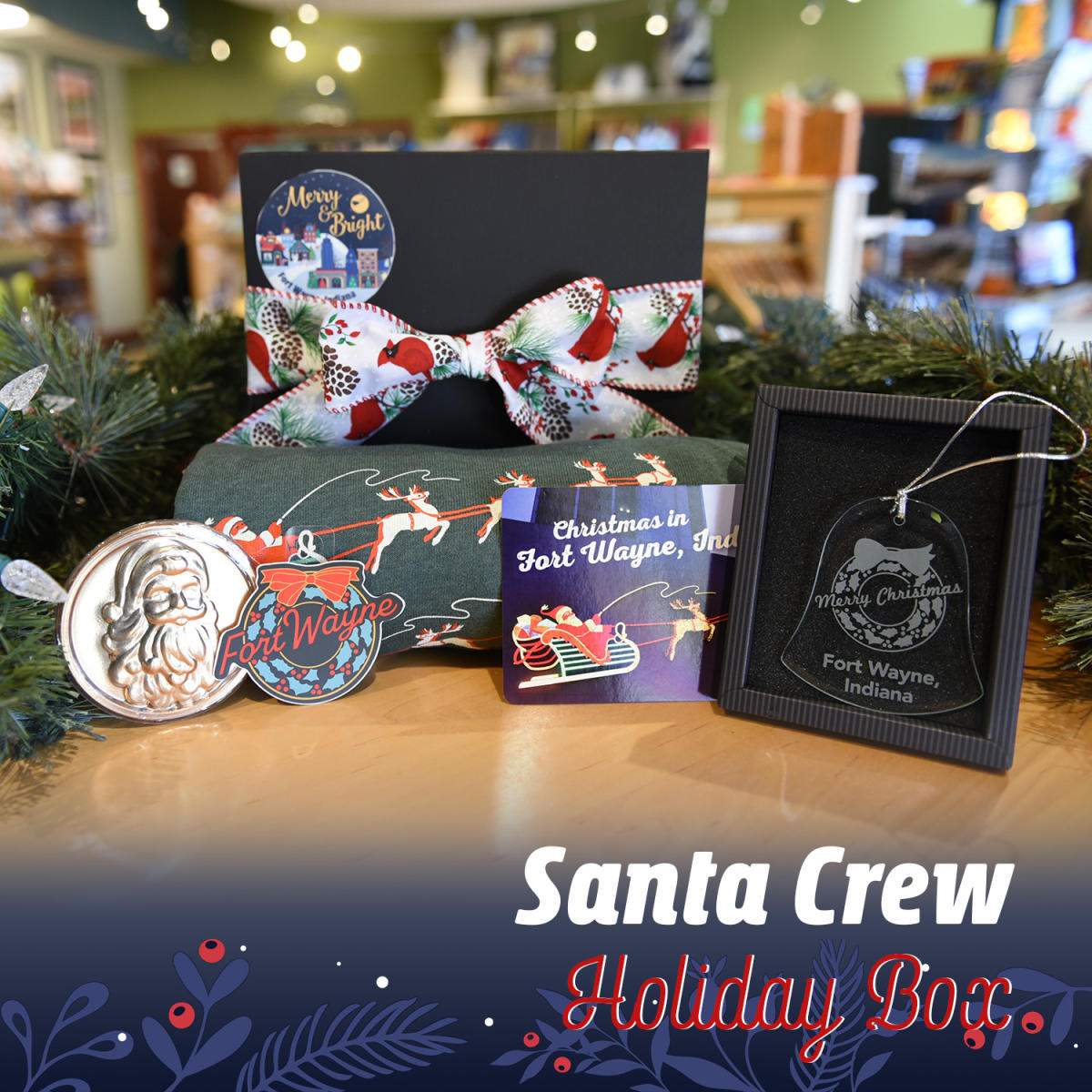 Gift box showing items including a green crew neck sweater and post card with the Fort Wayne Santa and his Reindeer lights downtown, a Santa chocolate bar, and a sticker and glass ornament of the Fort Wayne wreath light downtown.