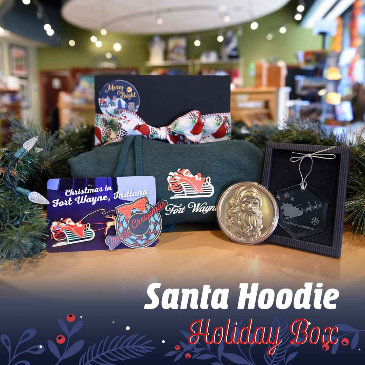 Gift box showing items including a green hoodie sweatshirt and post card with the Fort Wayne Santa and his Reindeer lights downtown, a Santa chocolate bar, and a sticker and glass ornament of the Fort Wayne wreath light downtown.