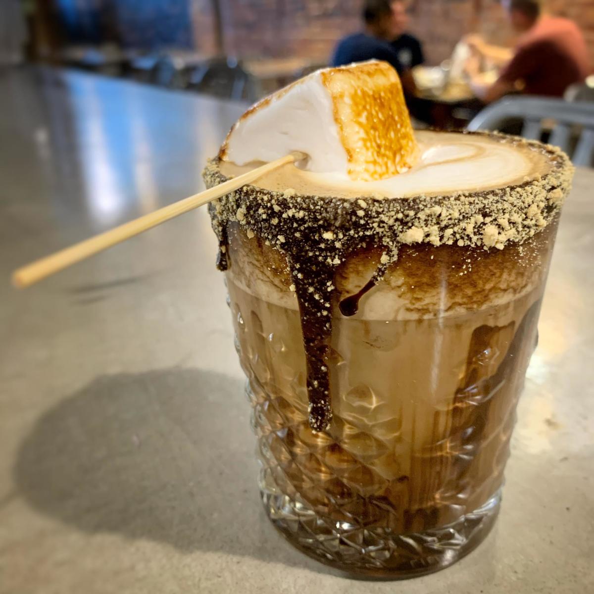 glass cup of coffee with chocolate and graham crackers on rim and giant marshmallow in foam