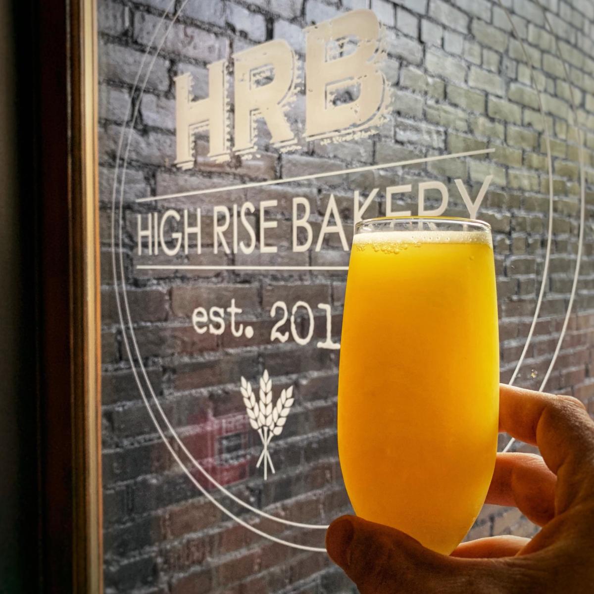 mimosa held up in front of High Rise Bakery logo