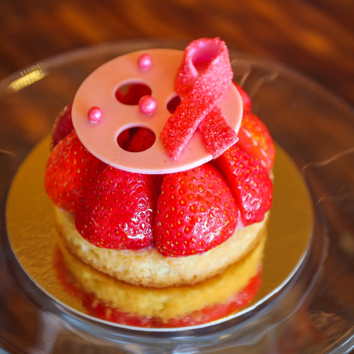 fotografía de cerca de una tarta de fresas con un listón rosa alusivo al cáncer de mama