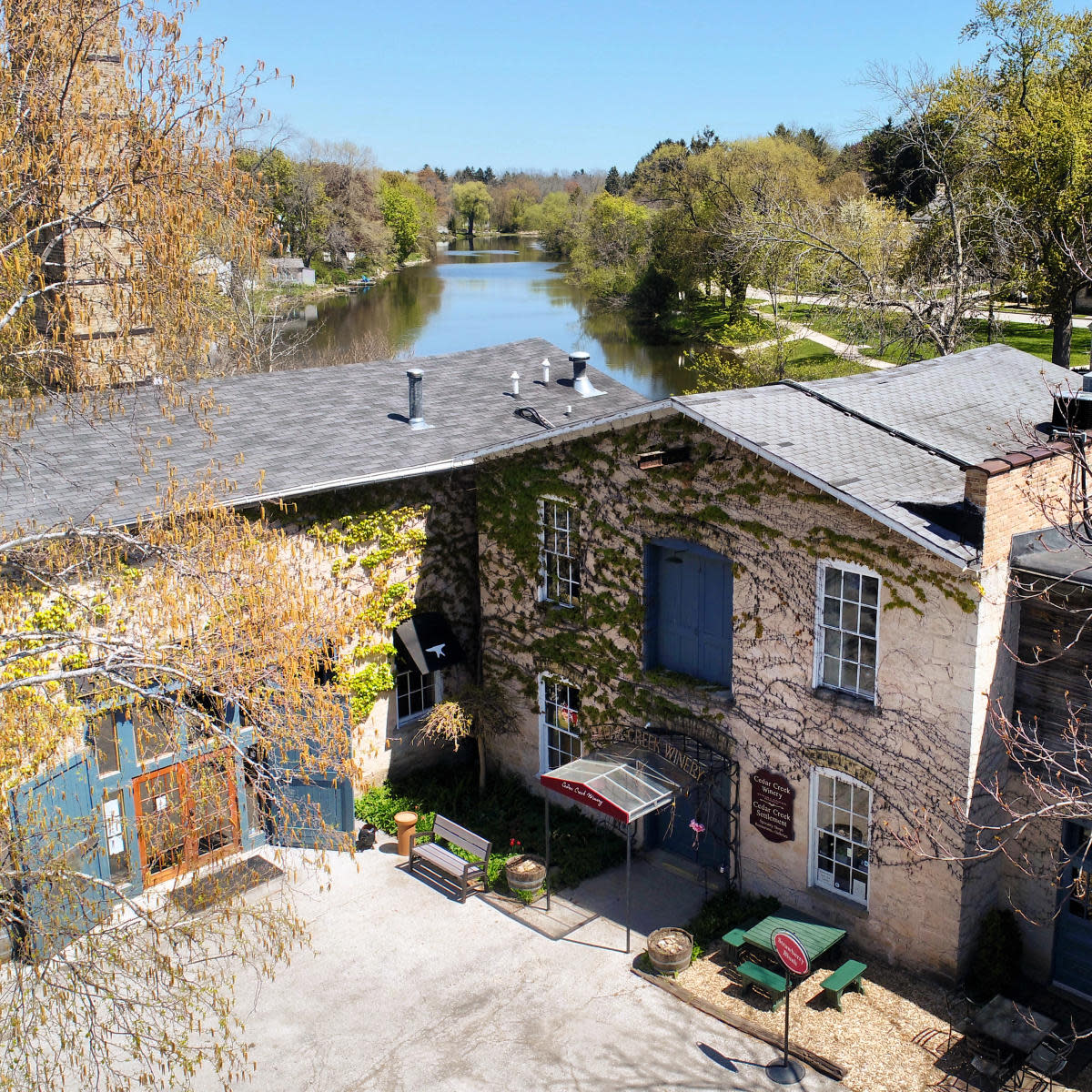 Cedar Creek Winery in Cedarburg, Wisconsin, with ivy-covered stone walls and a view of the river and trees on a sunny day.