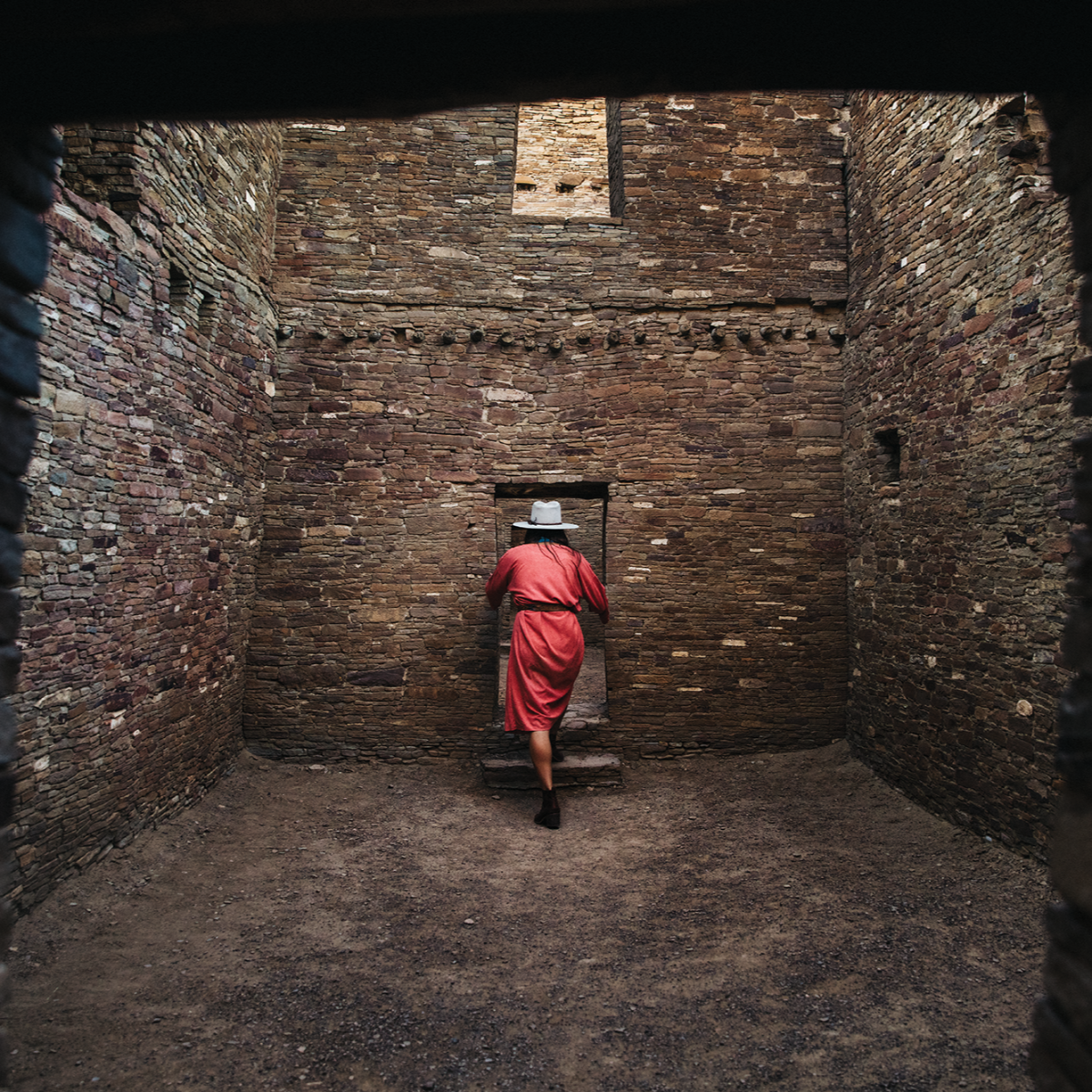 a person in a red dress enters a weathered stone doorway inside a stone room
