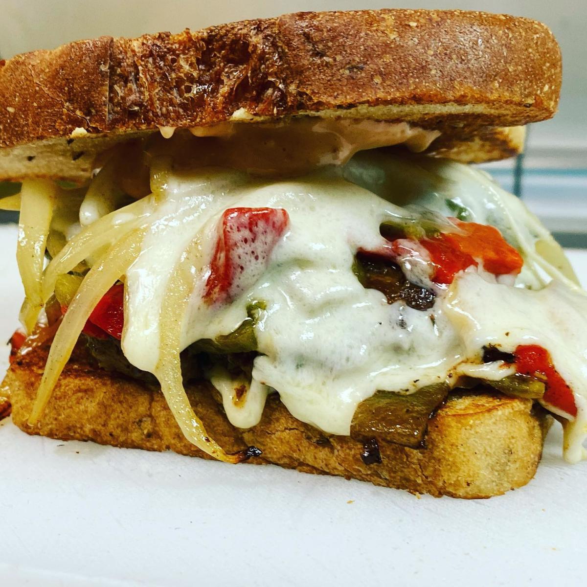 Grilled sandwich with melted cheese, sautéed onions, and bell peppers between toasted bread; golden, gooey, and appetizing.