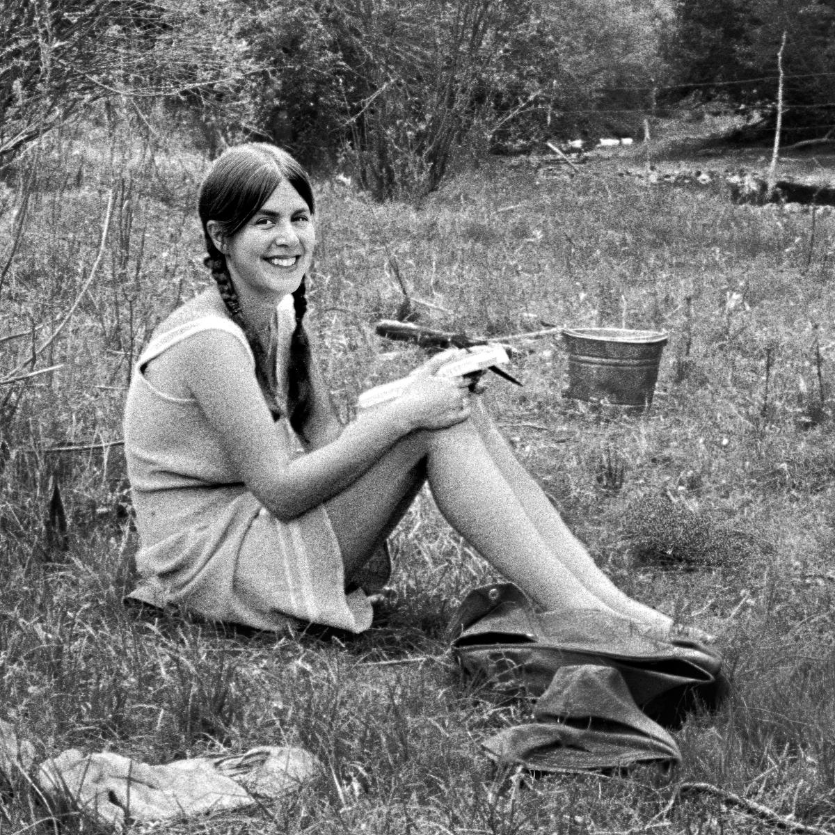 Black and white photograph of photographer Lynn Adler sitting on grass outdoors, smiling at camera.