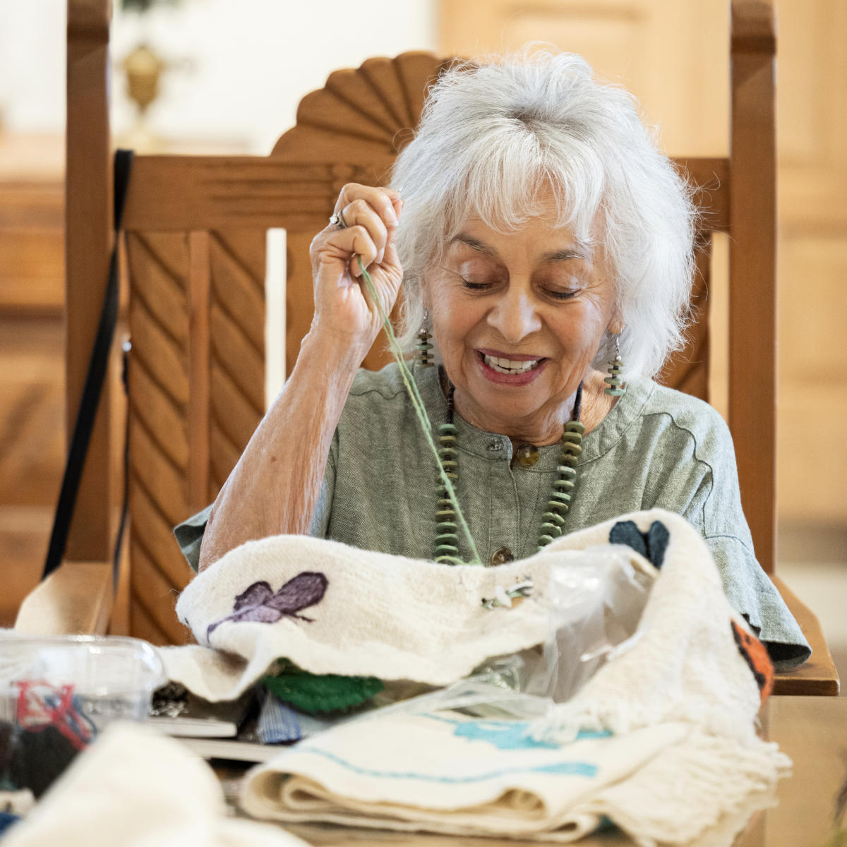 Person working on a textile piece with embroidered designs, seated at a table.