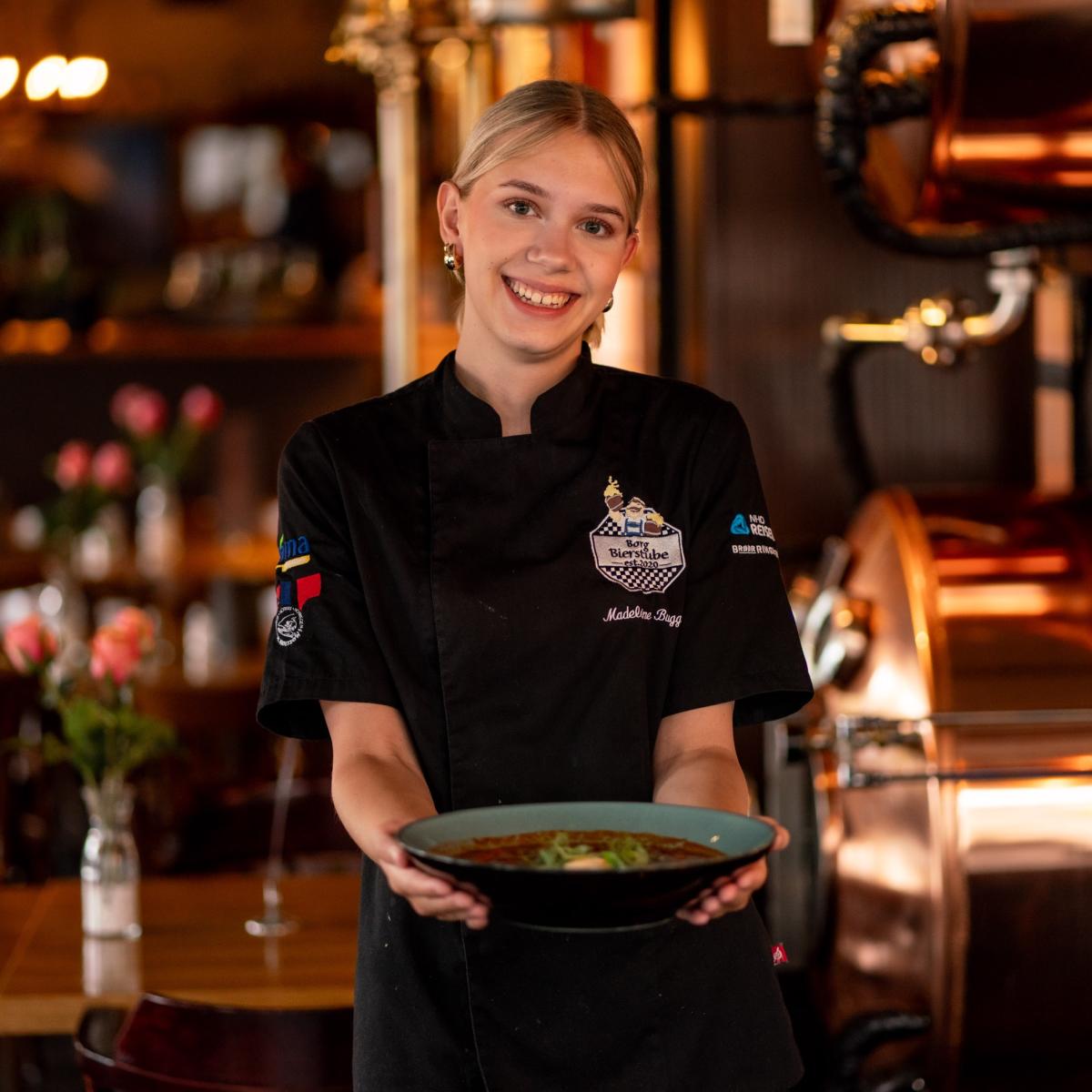 Smilende ansatt med en tallerk i hendene på Borg Bierstube i Sarpsborg. Foto.