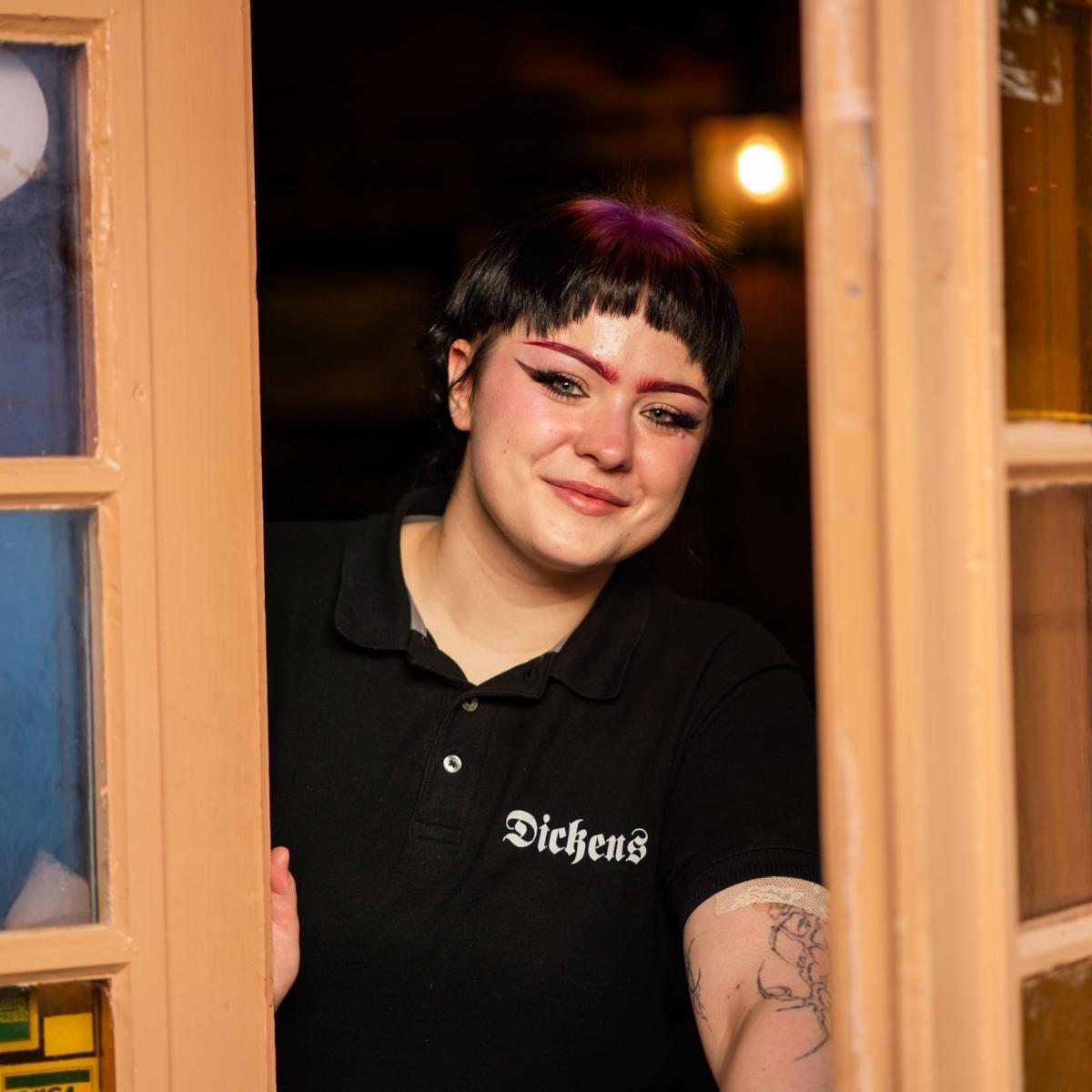 Smilende ansatt i døren hos Dickens i Sarpsborg. Foto.