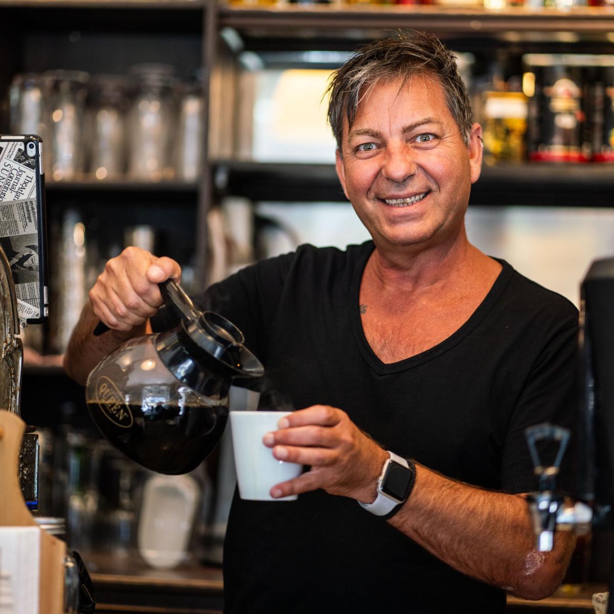 Smilende mann som sjenker kaffe i en kaffekopp hos Kaffeforretningen Sarpen. Foto.