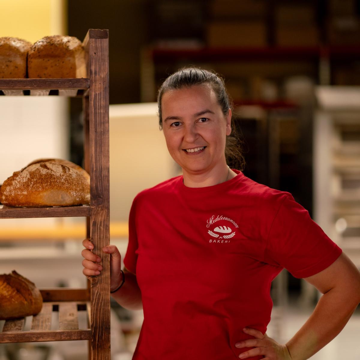 Smilende kvinne som holder i en hylle med brød. Foto.