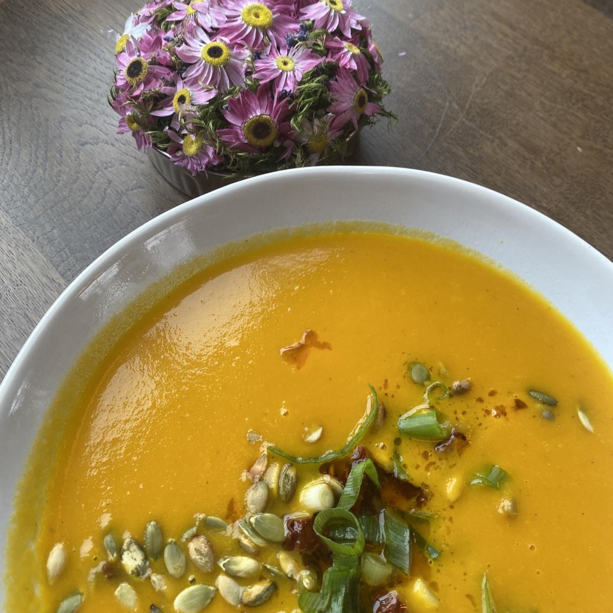 Nærbilde av en tallerk med gul suppe og gresskarkjerner. Foto.